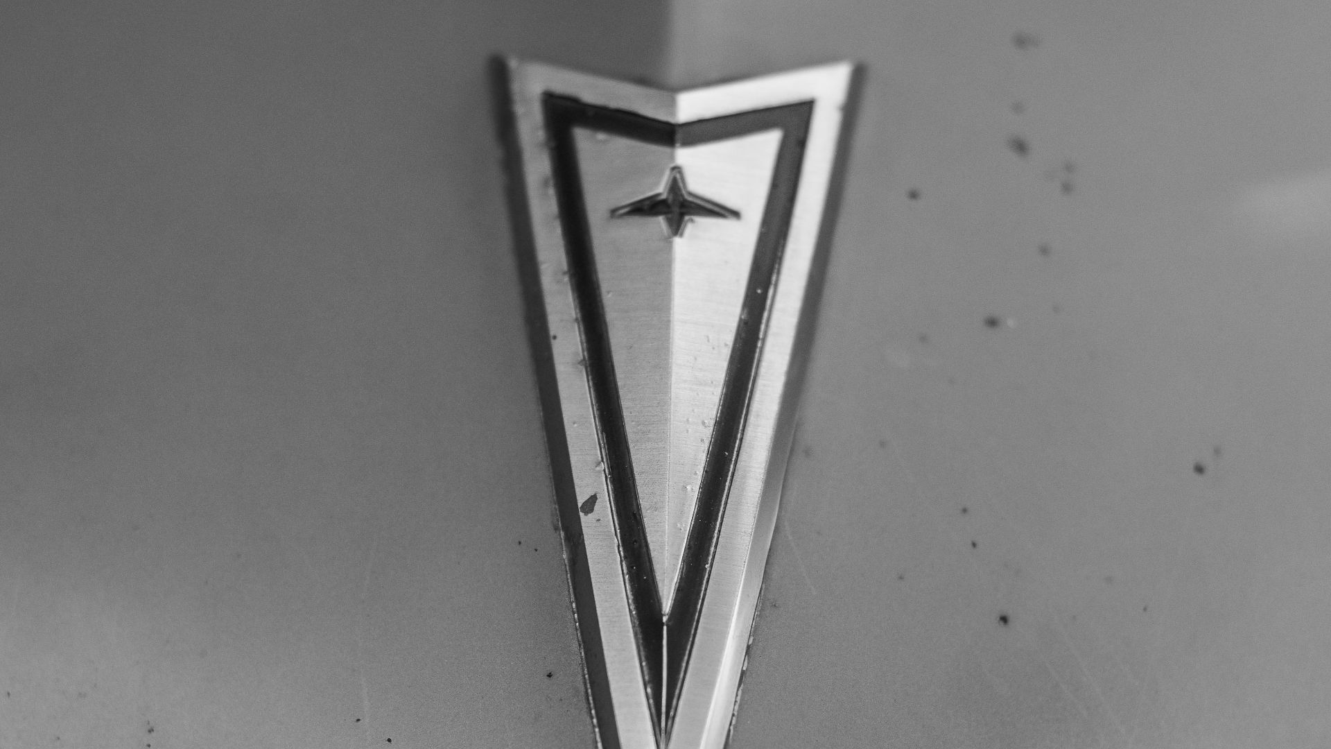 Black and white close-up of a classic Pontiac emblem on a vintage car hood, showcasing chrome details.