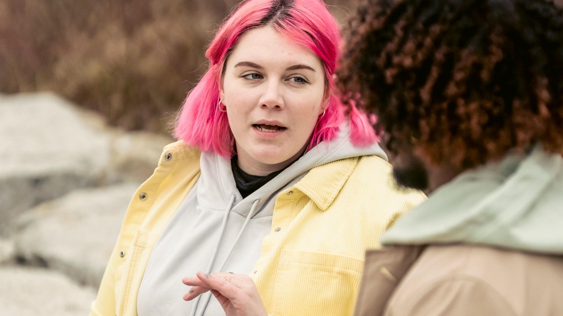 Plump woman with pink hair having conversation with faceless African American man while sitting on stones with cans of soda