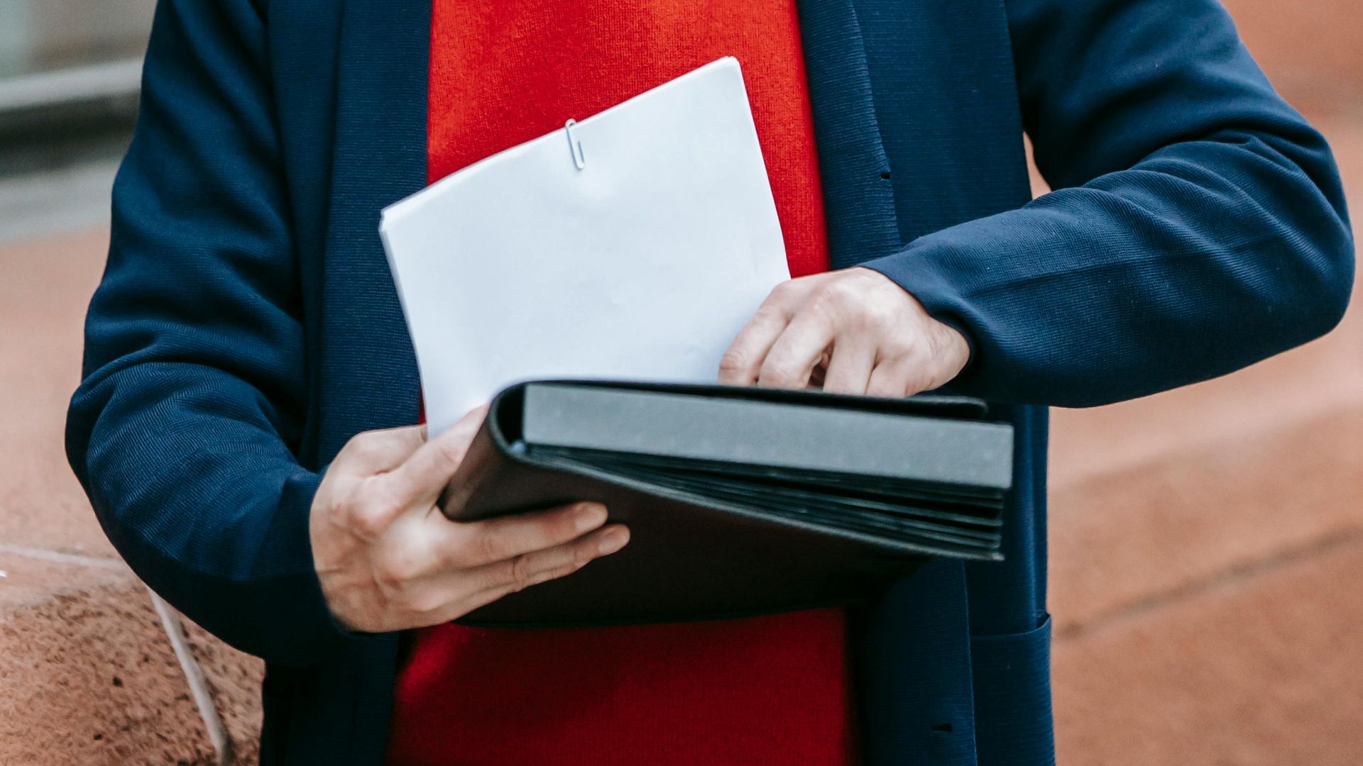 A man dressed in formal attire examines papers outside a building.