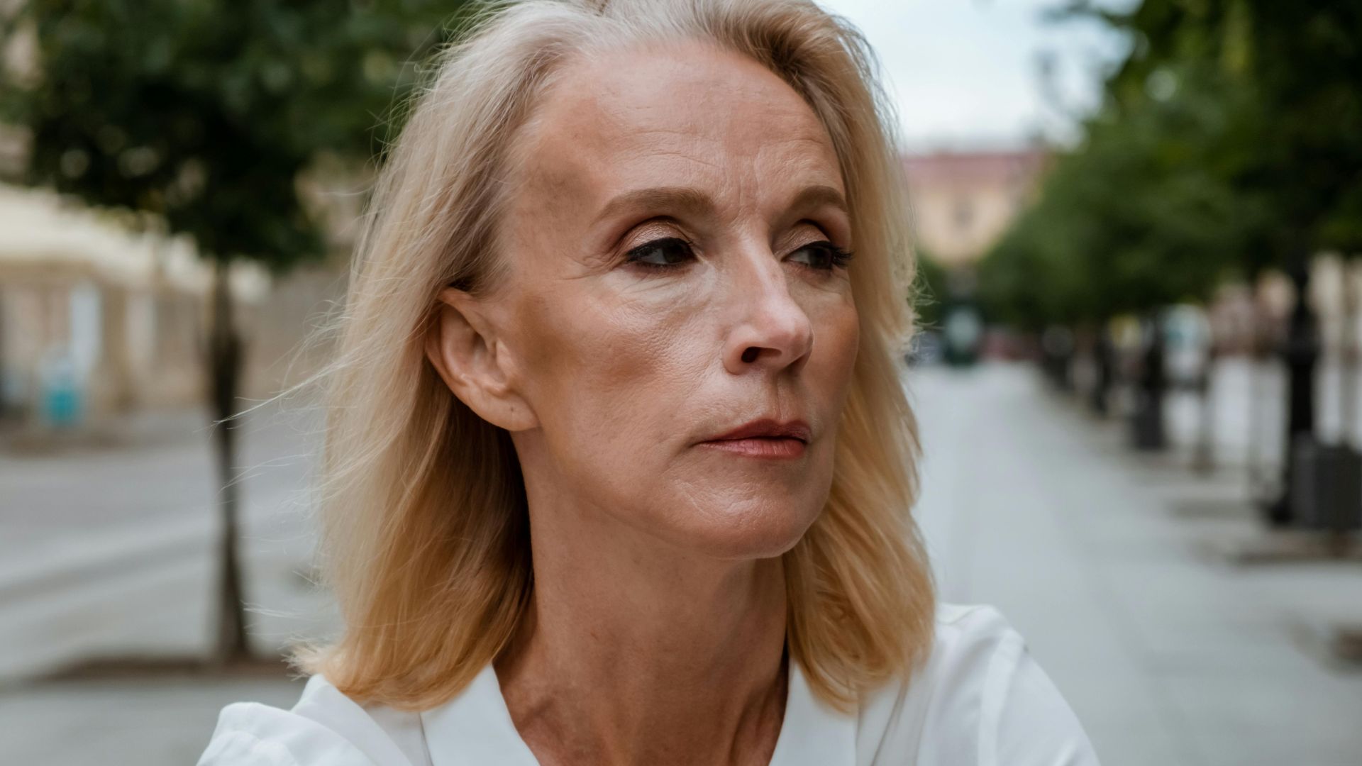 Senior woman wearing a white shirt poses thoughtfully on a quiet city street.
