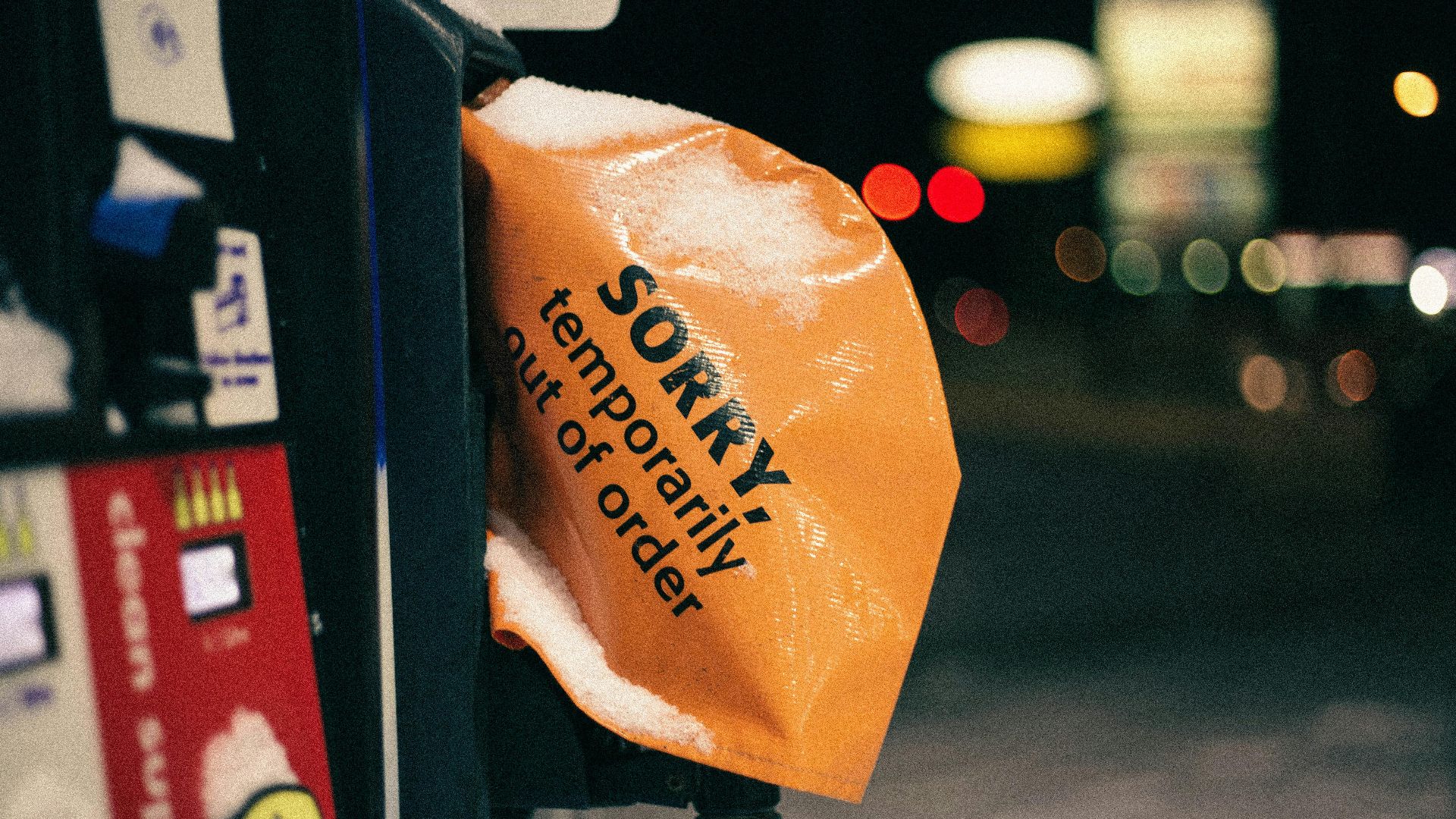 A covered fuel pump in winter with a 'temporarily out of order' sign at night.