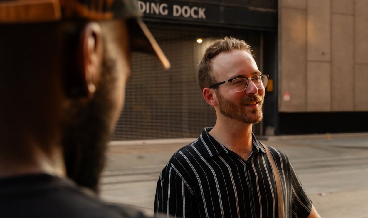 A man in a black shirt and glasses talking to another man
