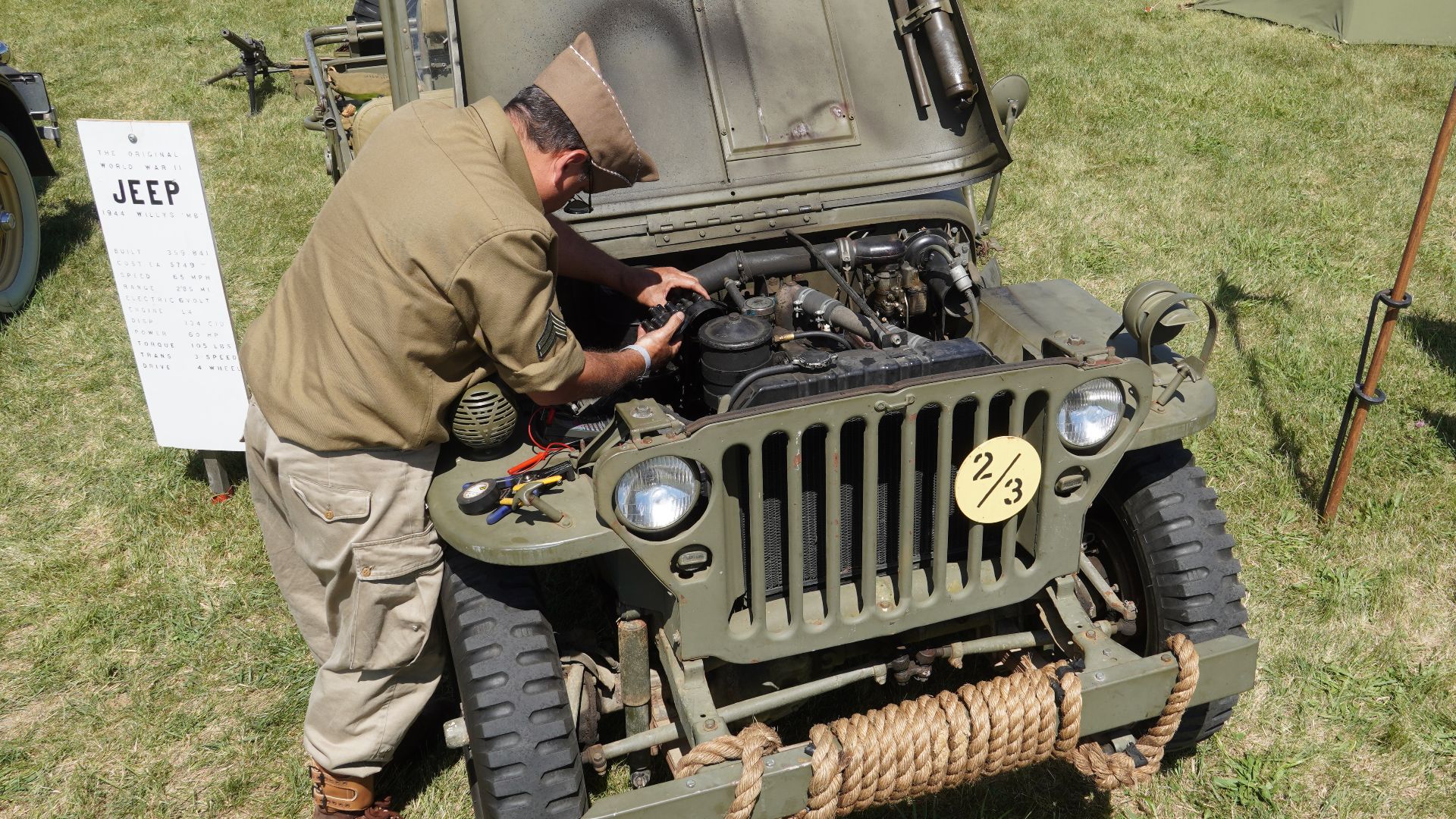 a 1944 Willys MB with its hood open, being inspected by a man in WW2 military clothing during WW2 Weekend at Reading Regional Airport