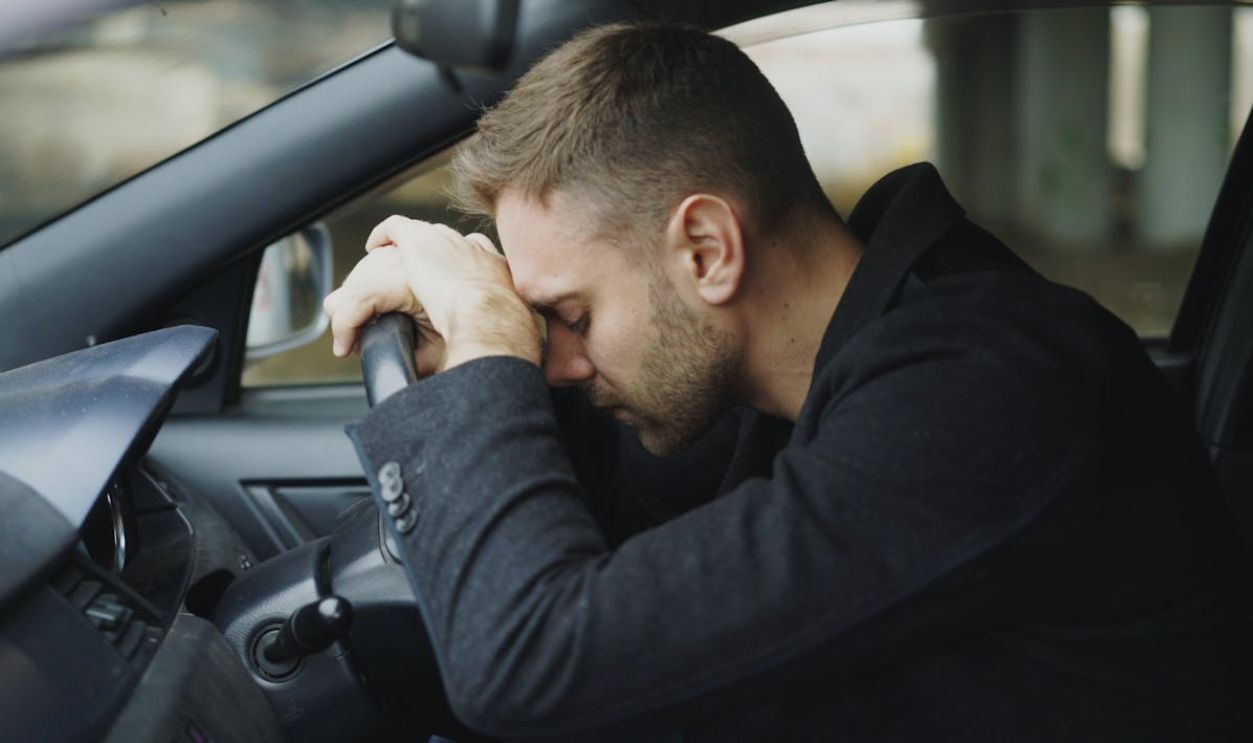 Stressed Man Resting on Steering Wheel in Car
