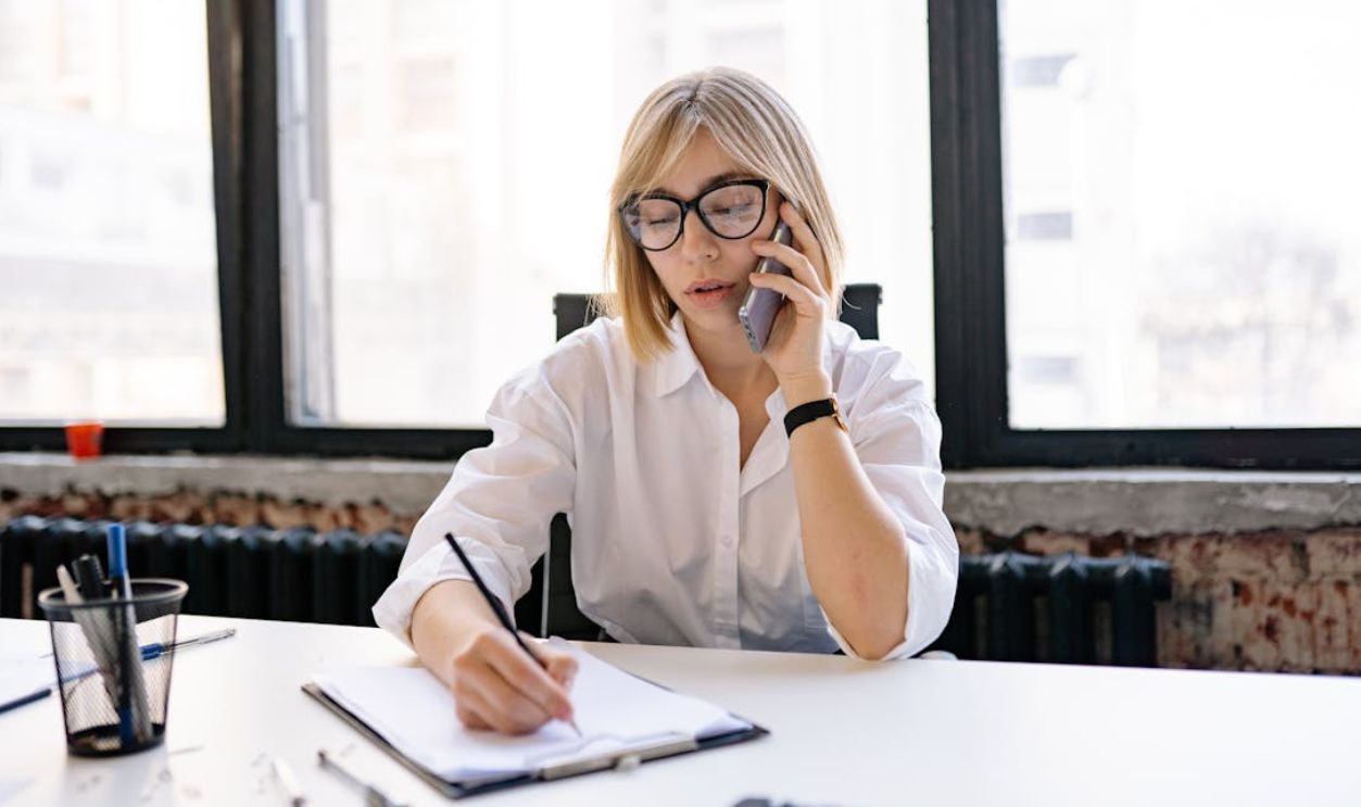 A Woman Writing Down Notes while Having a Phone Call