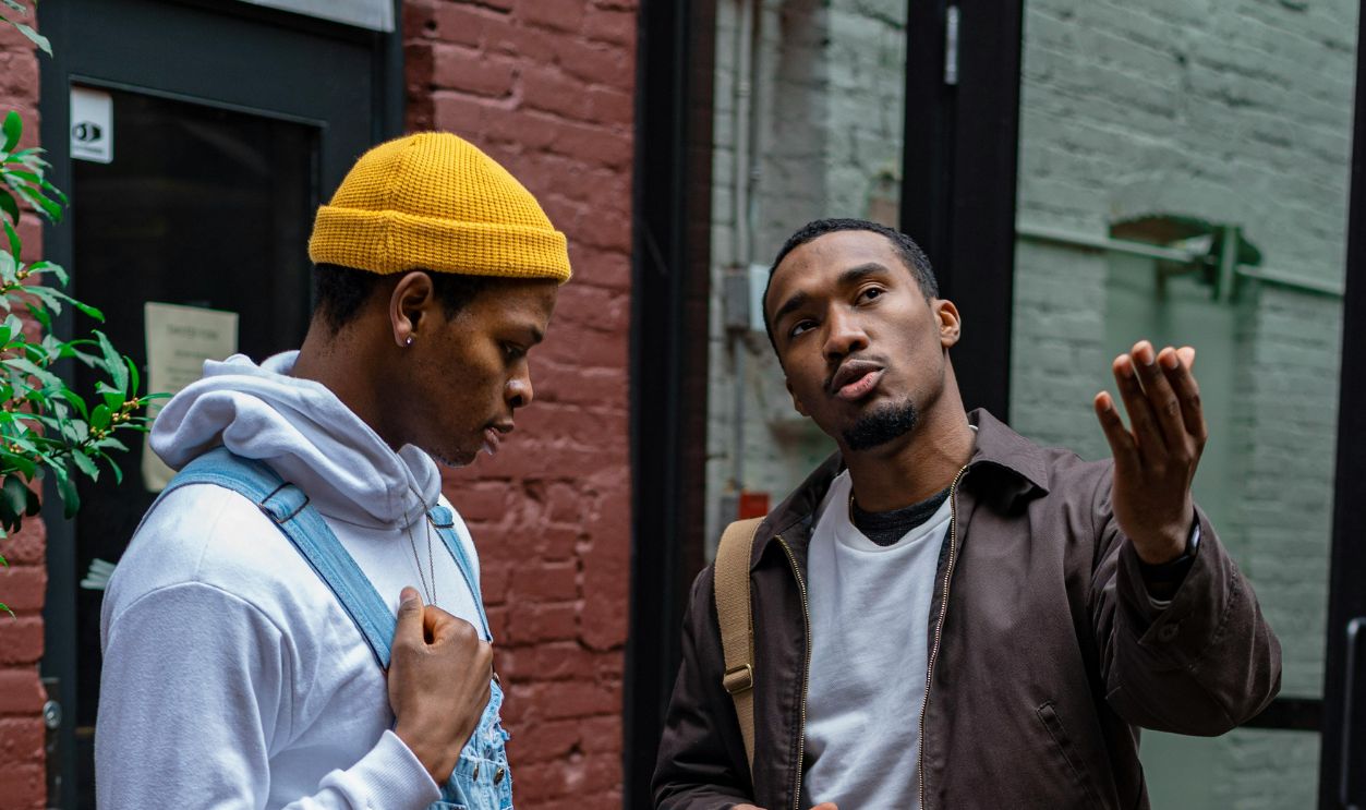 A Man in Brown Jacket Holding Camera Beside a Man with Yellow Knit Cap