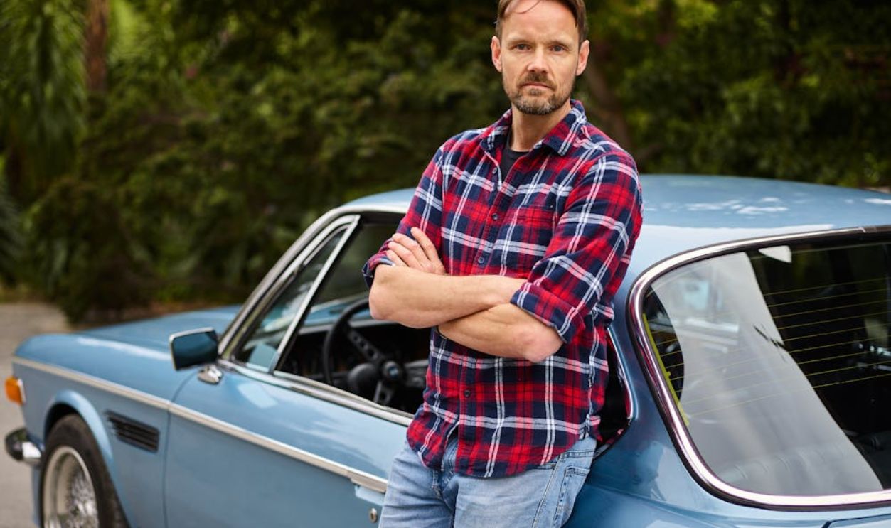 Calm man standing with folded arms near old car
