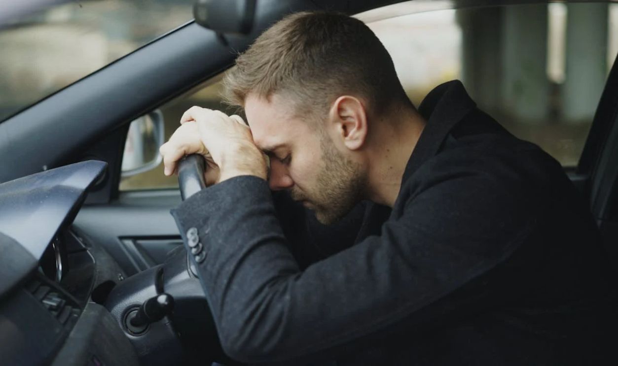 Stressed Man Resting on Steering Wheel in Car