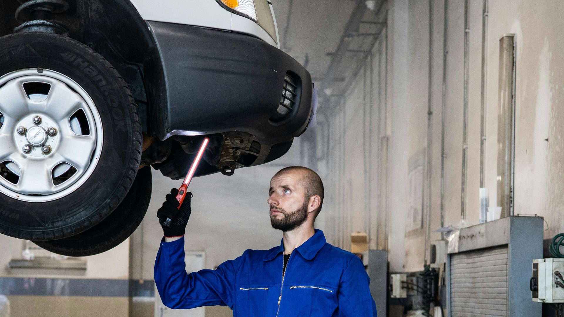 Mechanic in blue coverall inspecting car in auto repair shop. Professional vehicle maintenance in progress.