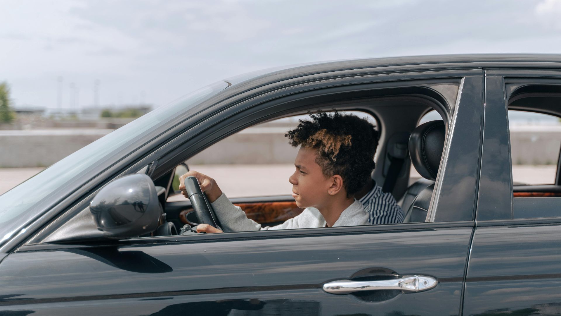 Side view of a young male teenager focused on driving a car in bright daylight.