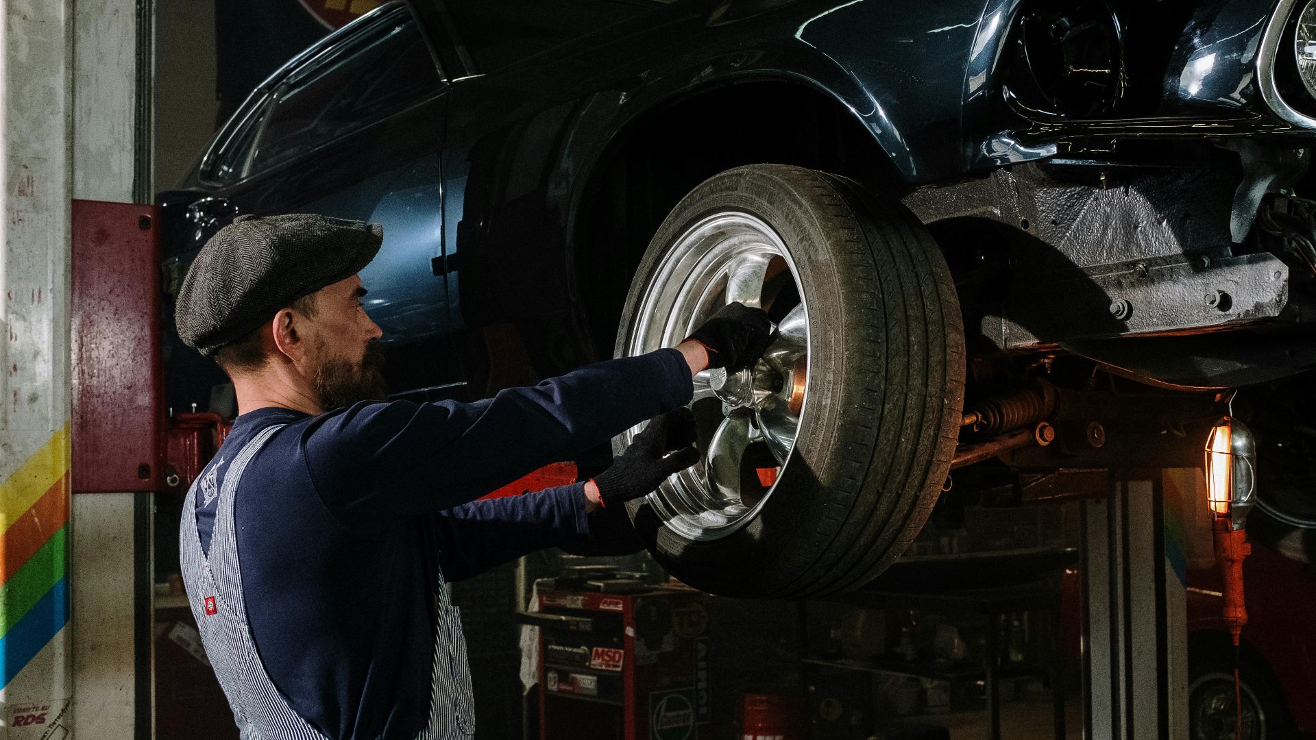 A focused mechanic works on a car wheel in a dimly lit garage, showcasing automotive repair skills.