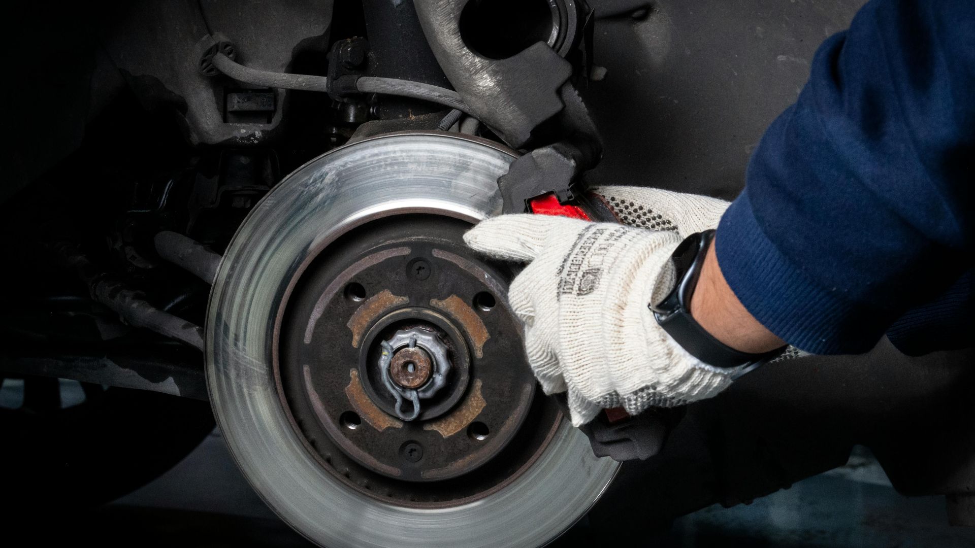 Mechanic working on car brake system in a workshop setting.