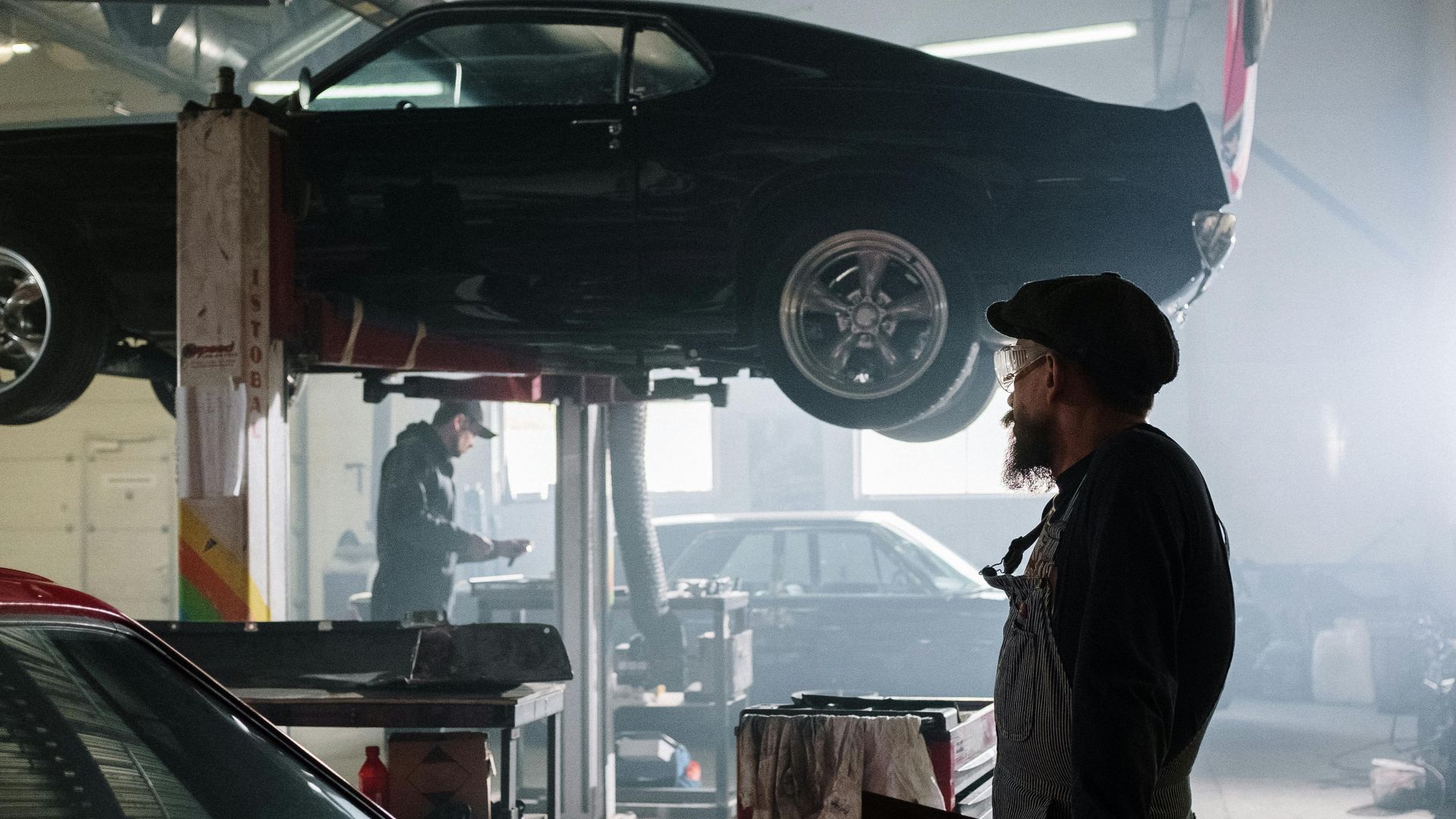 Mechanics busy at work in a dimly lit auto repair garage with a raised car.