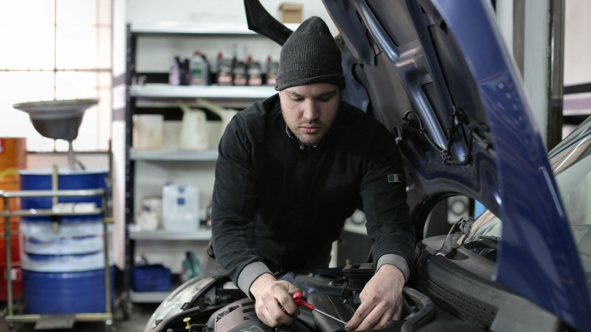 Man working under car hood in a garage, focused on engine repair