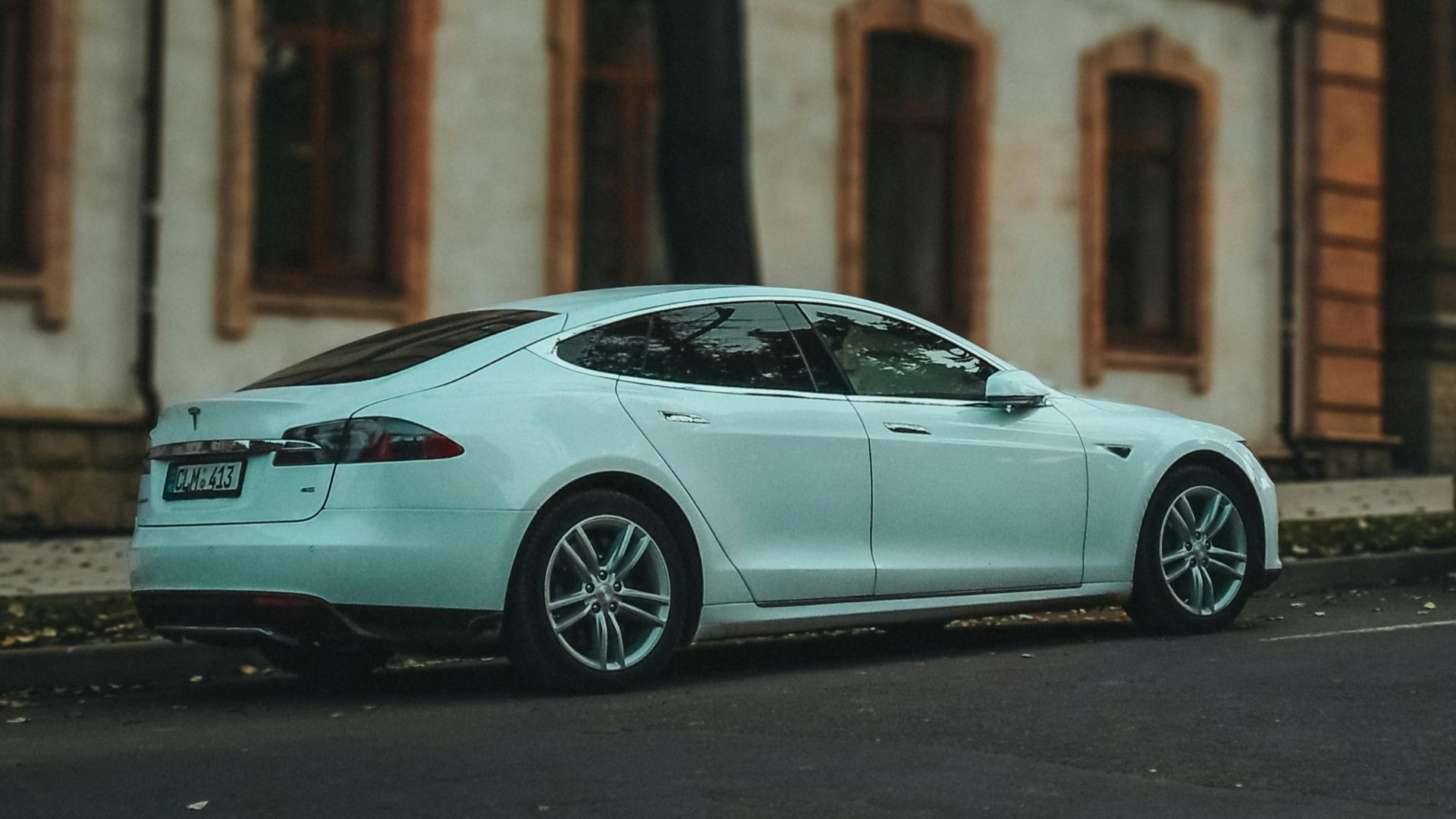 Side view of a sleek white sedan parked on a quiet urban street lined with trees.