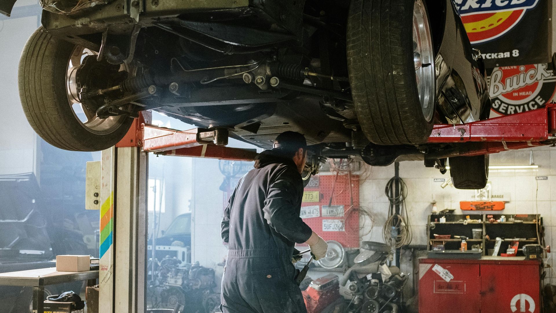 Mechanic repairing a vehicle in a busy workshop with various automotive tools.