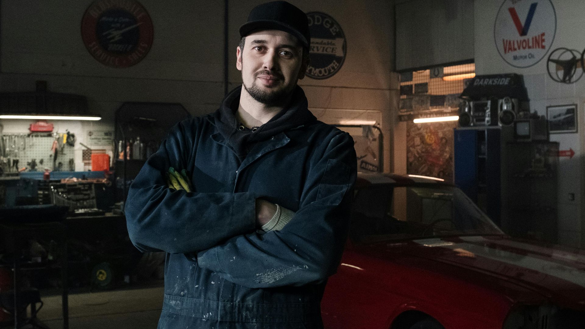 Experienced mechanic in a vintage garage standing confidently beside a classic car.