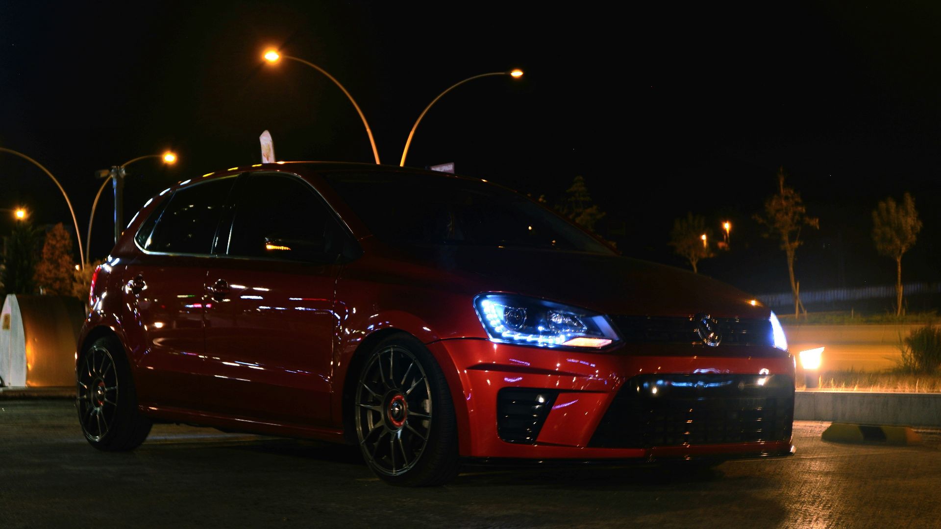 A red car parked in a parking lot at night