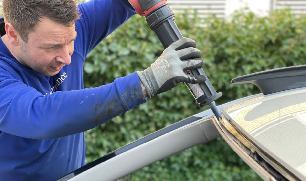 Man carefully applies glue to repair car windshield in Copenhagen outdoor setting.
