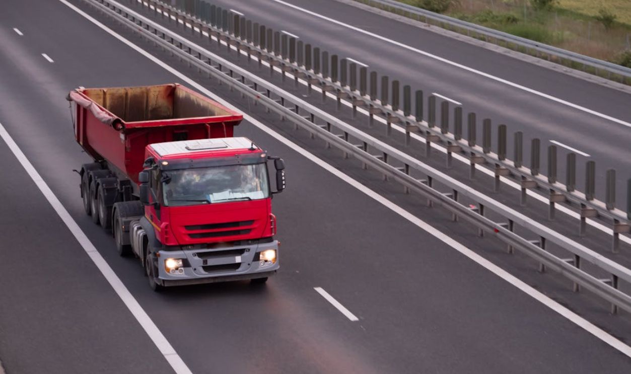 An overhead view of a red dump truck driving on an open highway during the day.