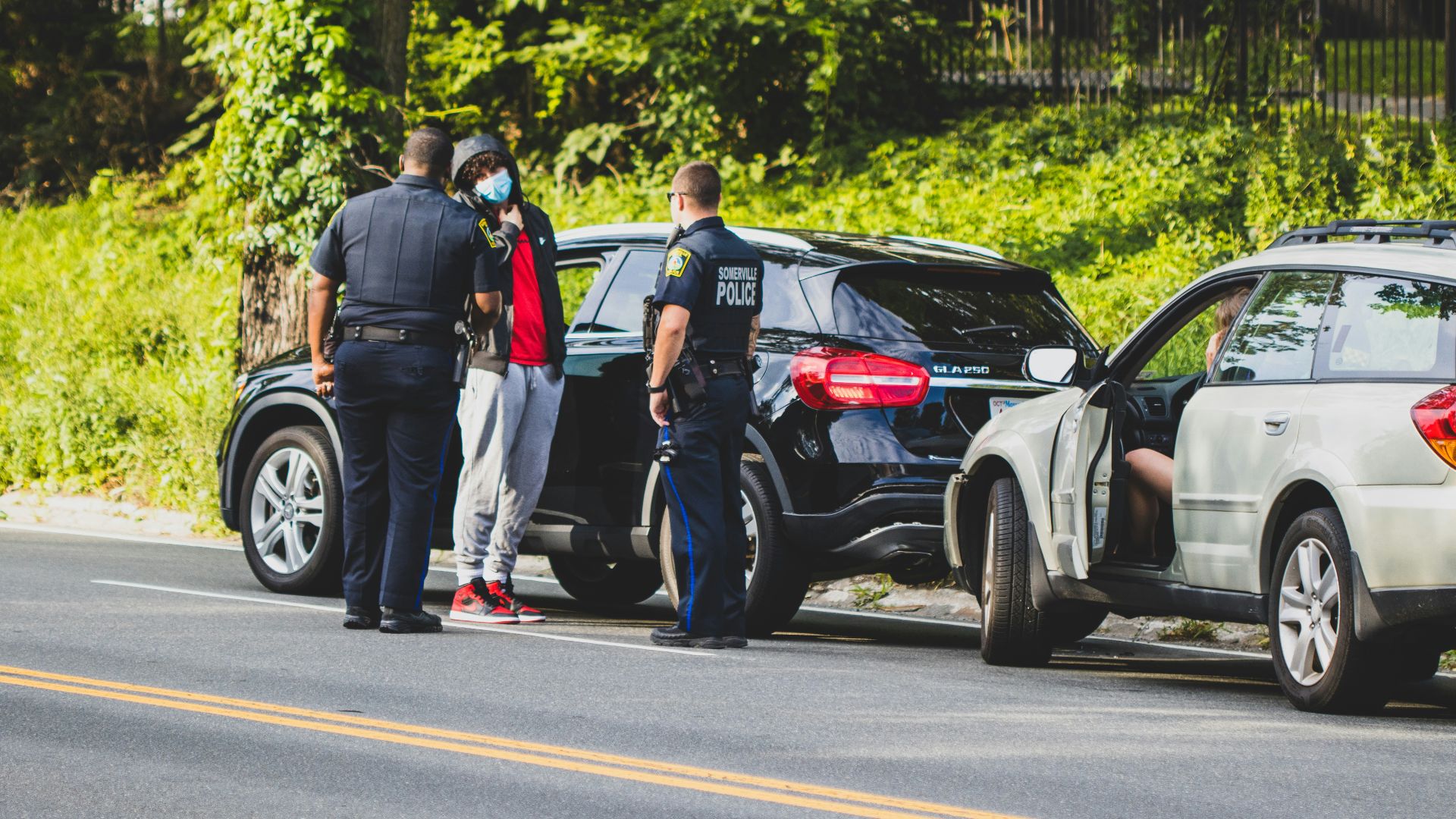 man in black t-shirt and black pants standing beside black suv during daytime