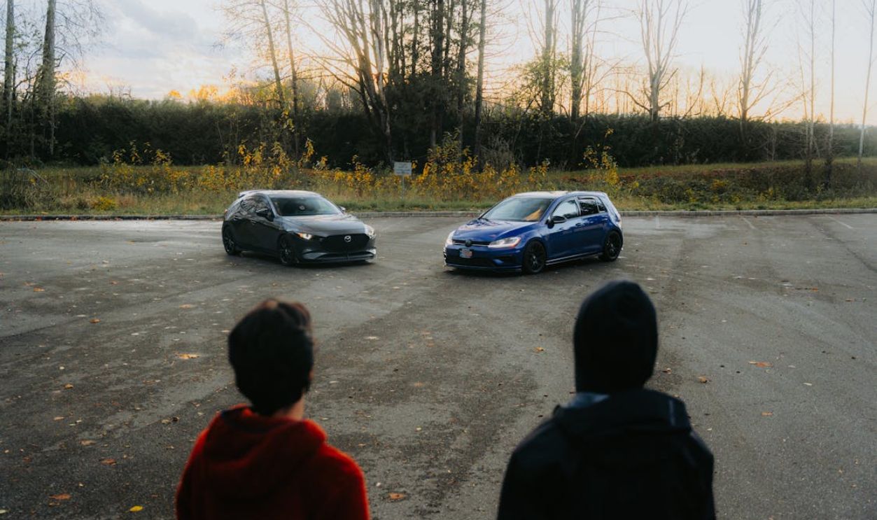Two adults observing parked cars in an open outdoor area during late afternoon.