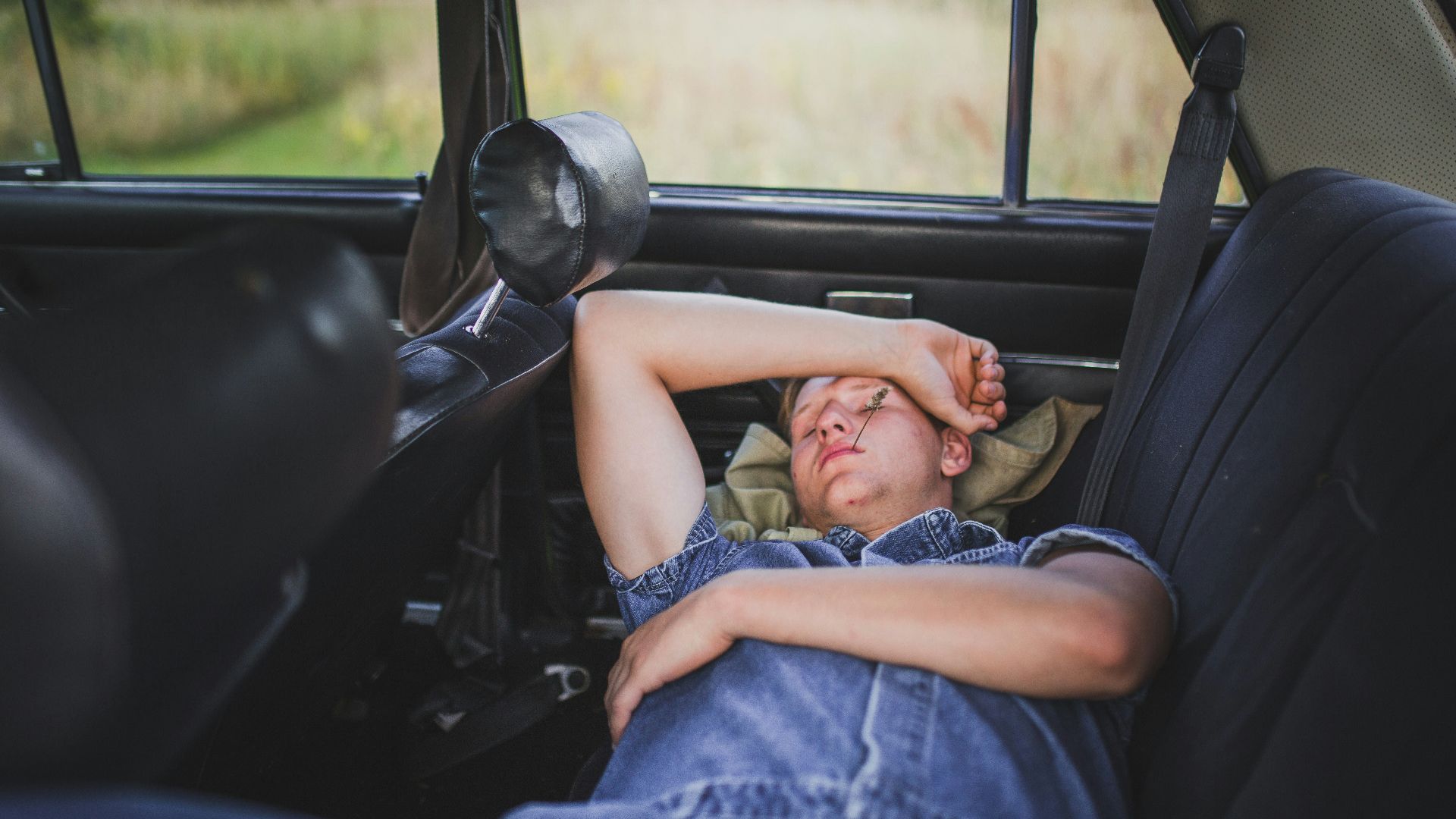 person in blue denim shirt sleeping behind the car seat