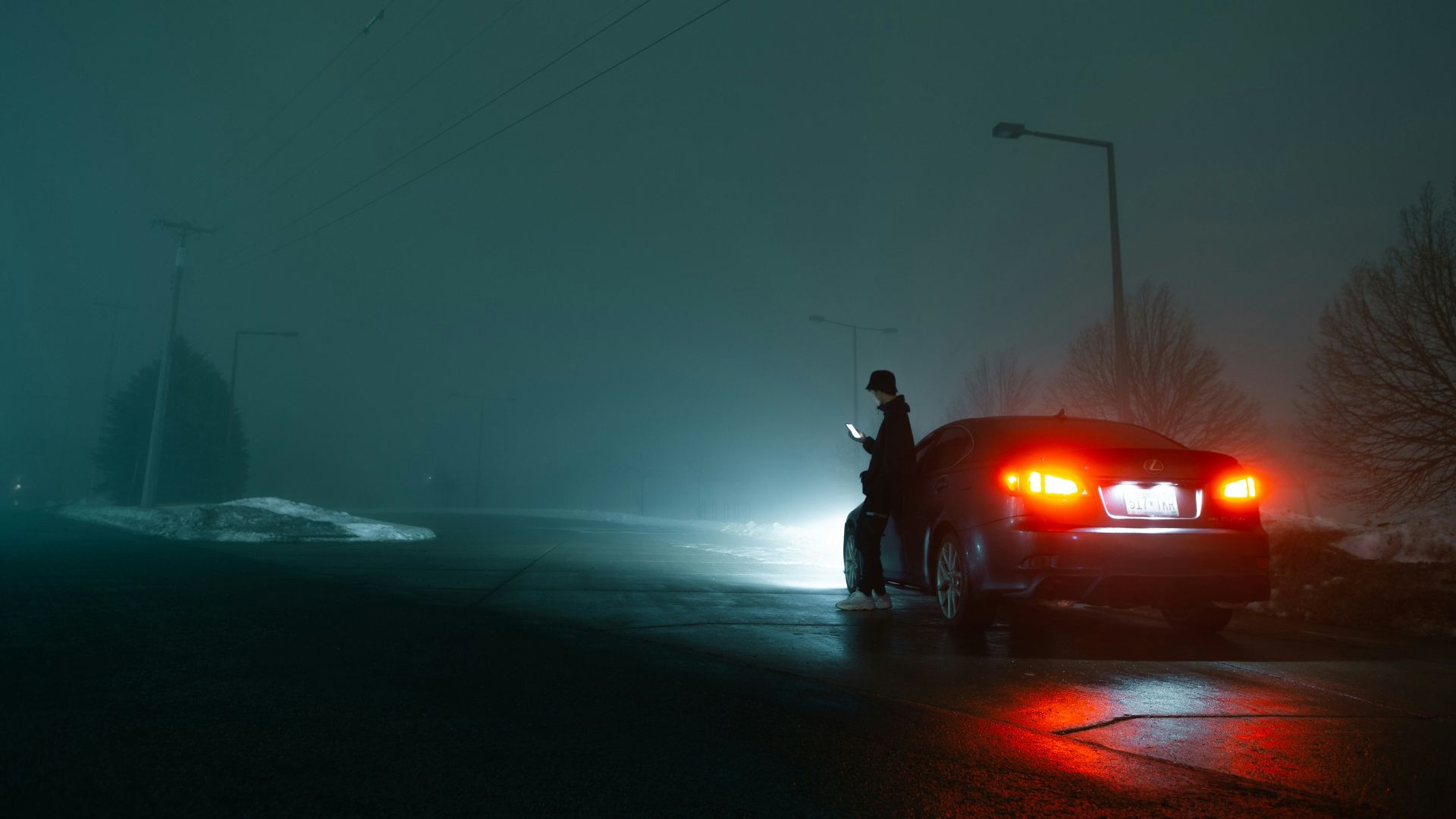 man in black jacket and black pants standing beside red car during night time