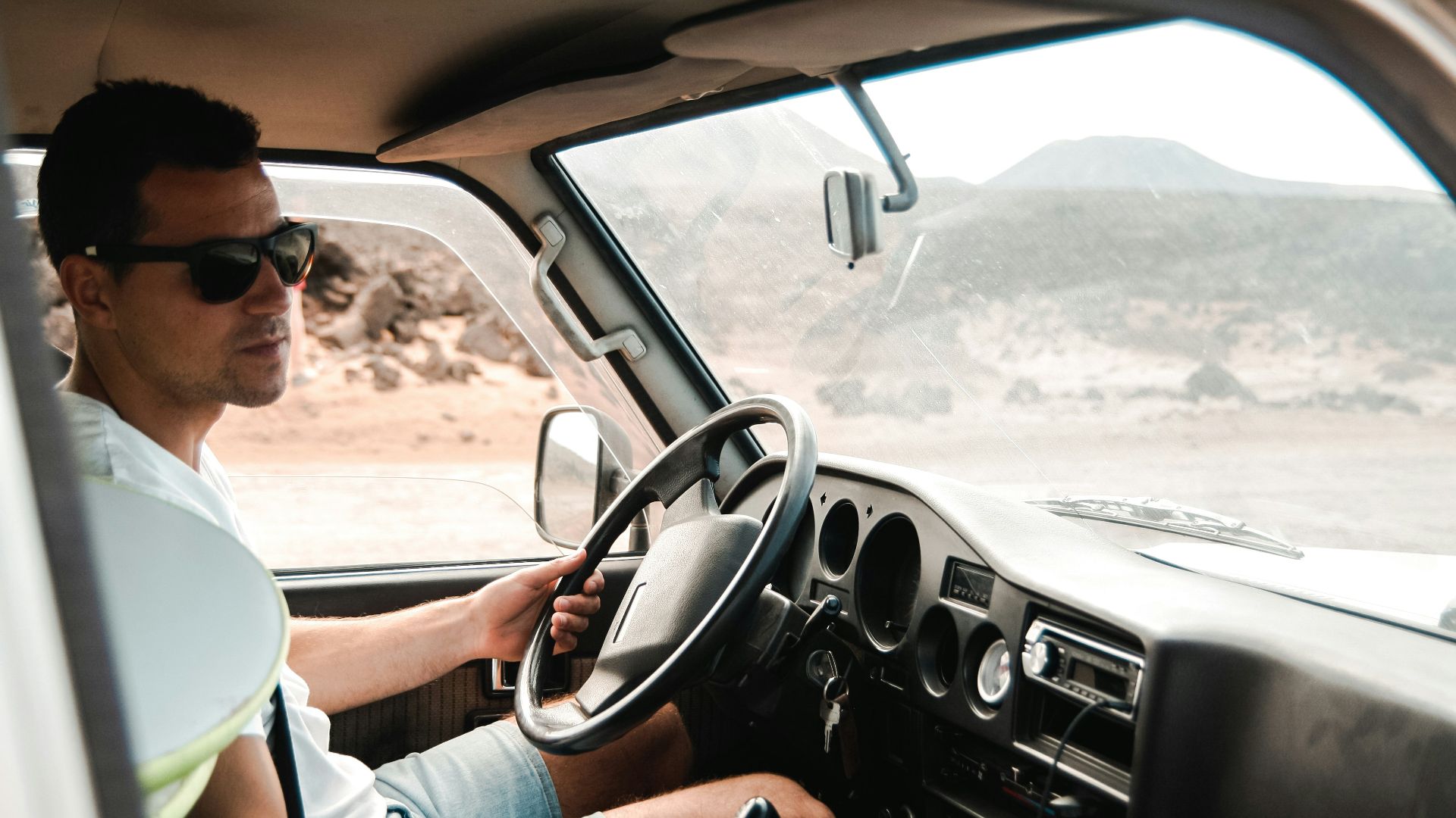 man wearing white crew-neck shirt holding steering wheel