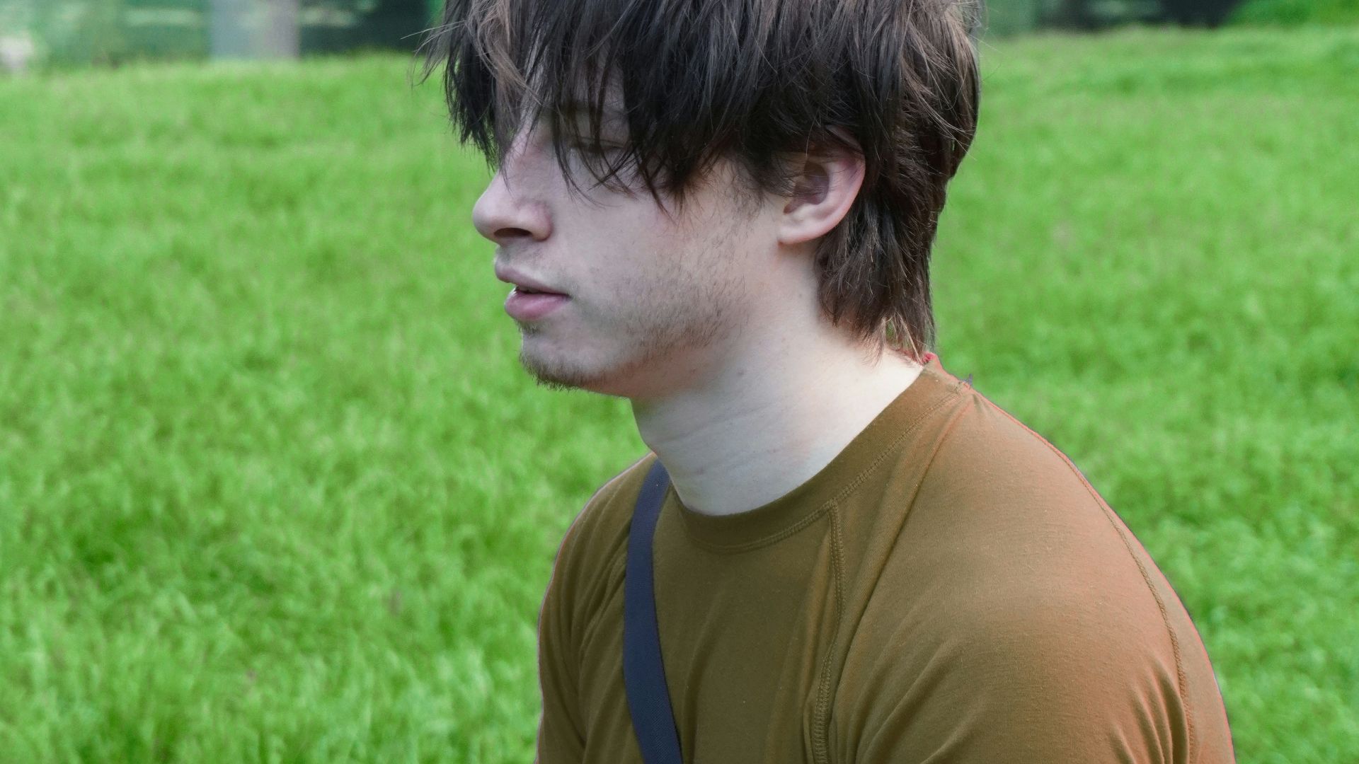 a young man sitting on the grass in front of a bridge