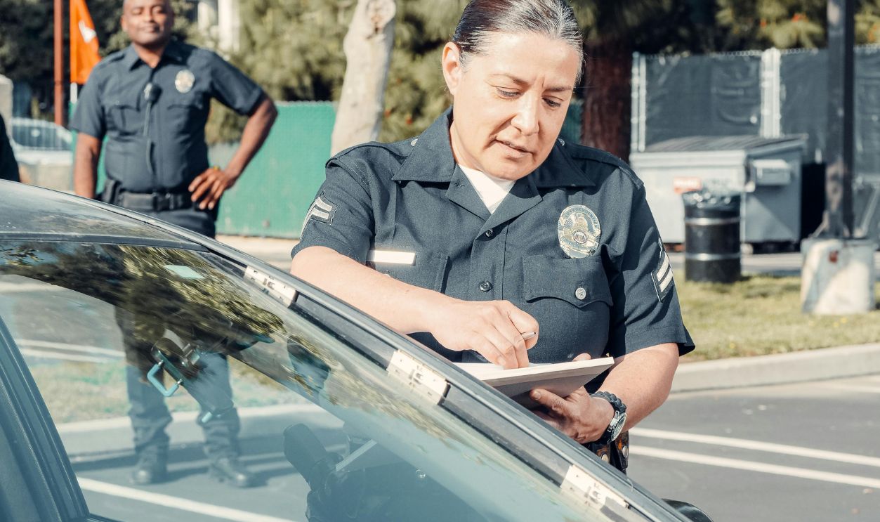 Police officers handling a traffic violation in a parking lot, focus on policewoman writing a ticket