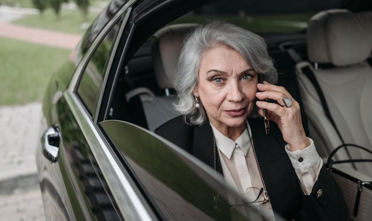 Confident senior businesswoman communicating on smartphone while seated in a luxurious car interior