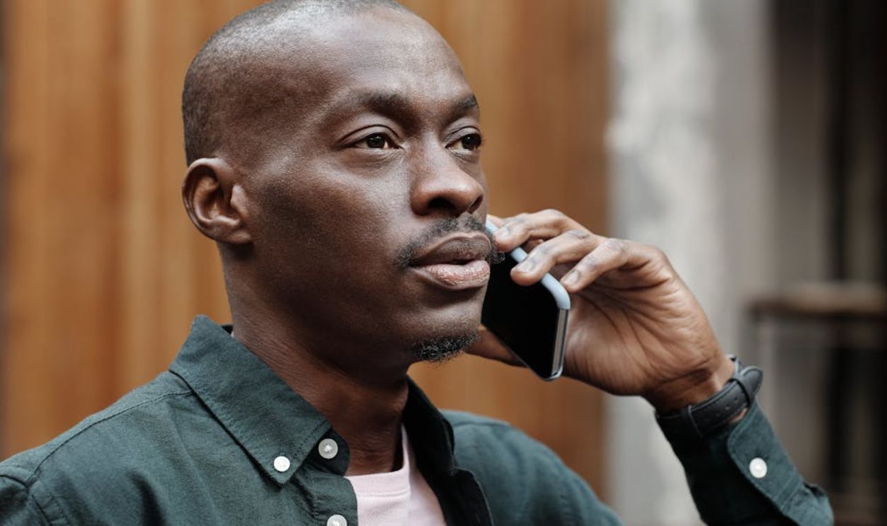 A stylish African American man in a shirt conversing on a smartphone outdoors