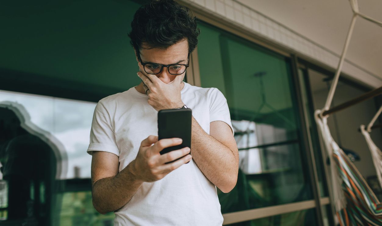 Man with eyeglasses focused on smartphone indoors, captured in a contemplative moment.