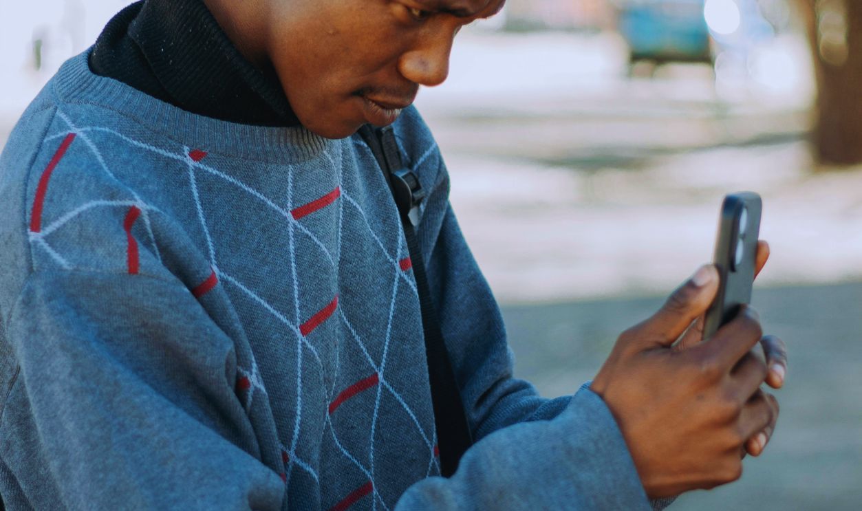 Casual young man interacting with smartphone outdoors in bright sunlight