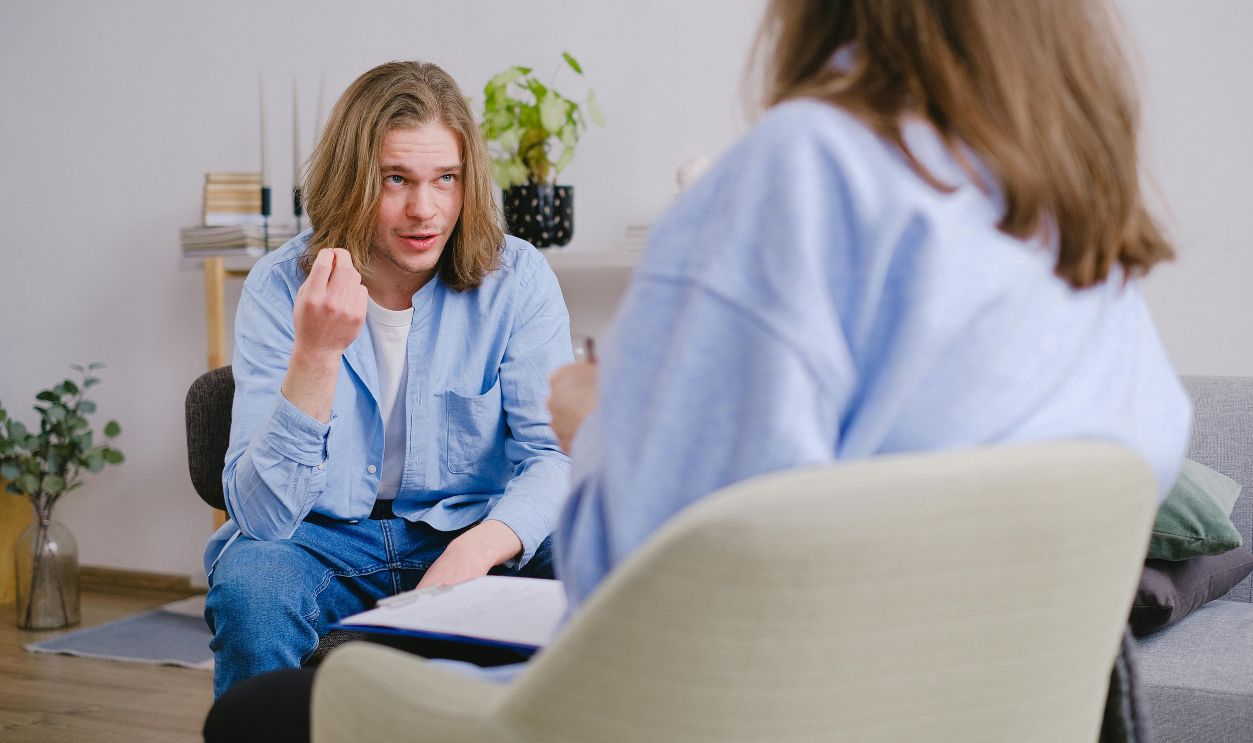 A young man in therapy, gesturing towards therapist in a comfortable setting