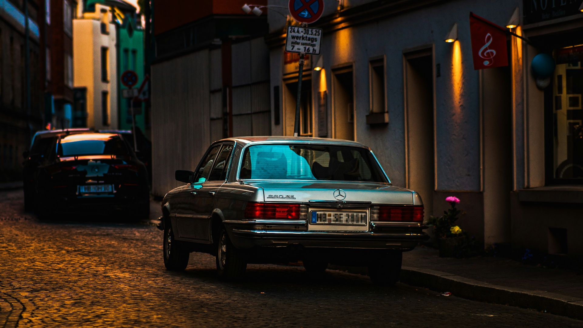 A silver car is parked on a cobblestone street.