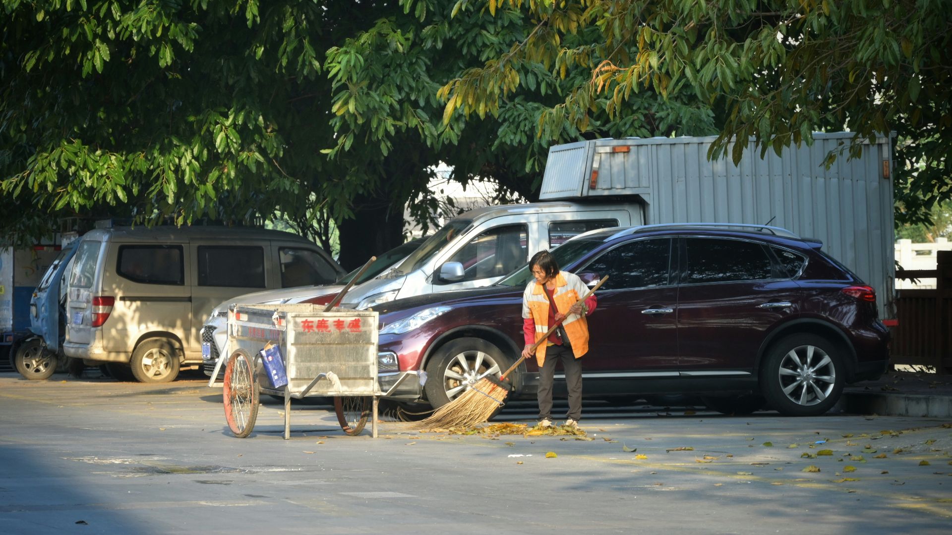 Person sweeping street near parked cars