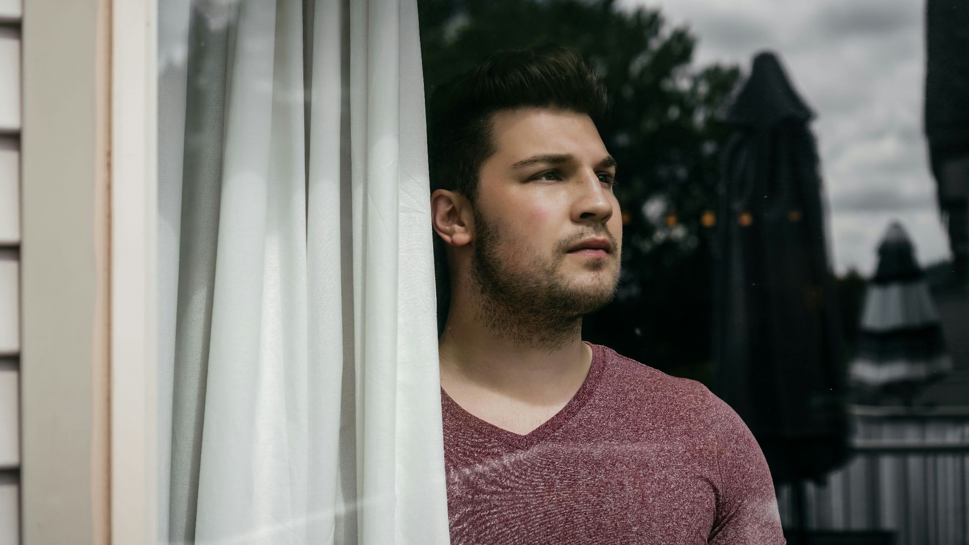 man in red crew neck shirt standing beside white curtain