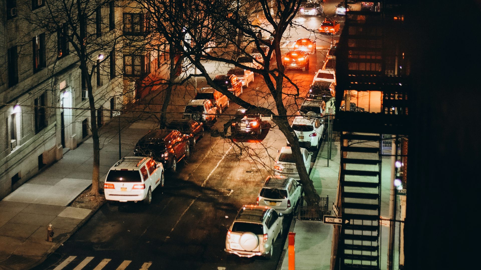 a city street at night with cars parked on the side of the road