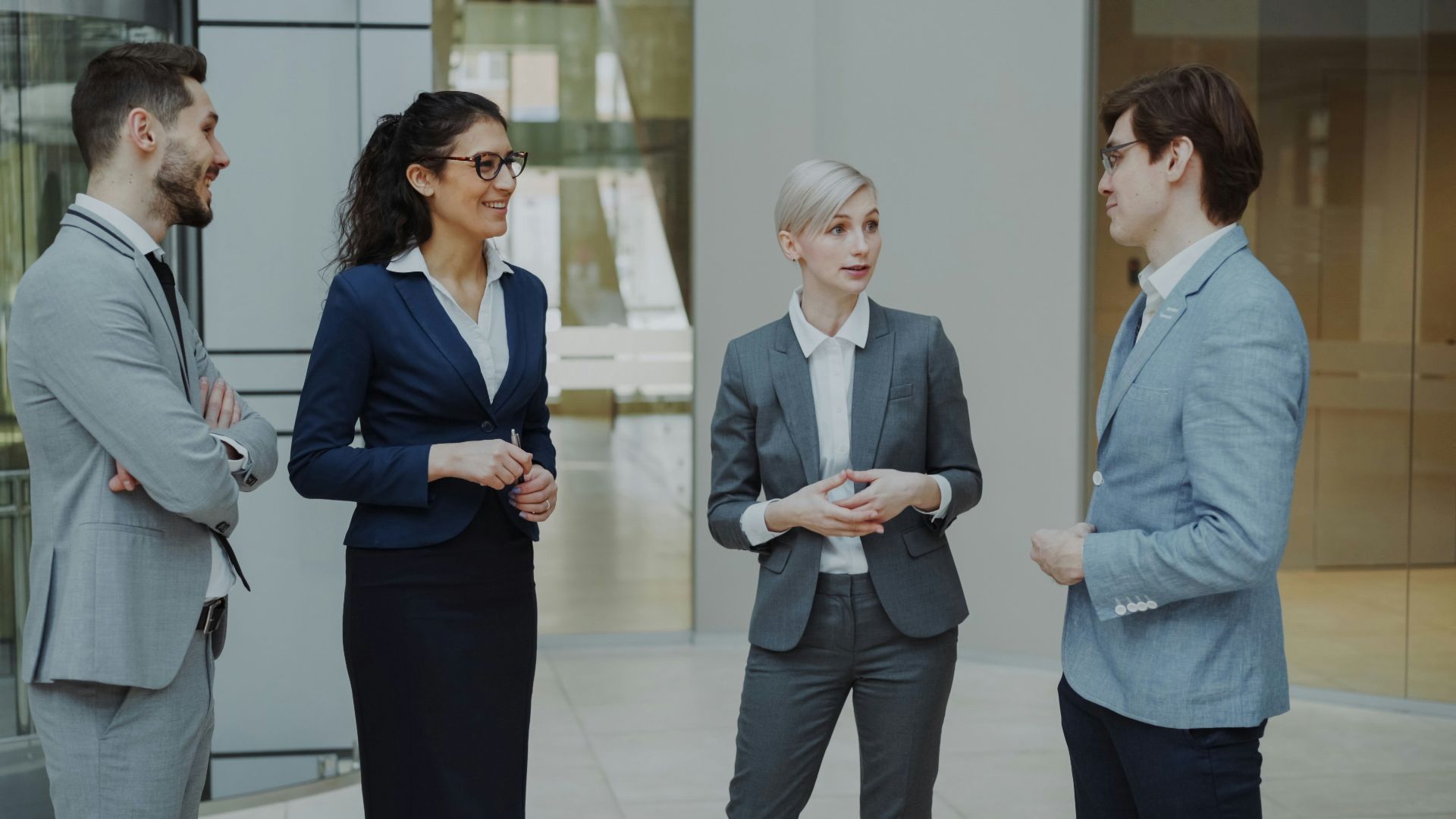 Four business professionals conversing in a modern office lobby.