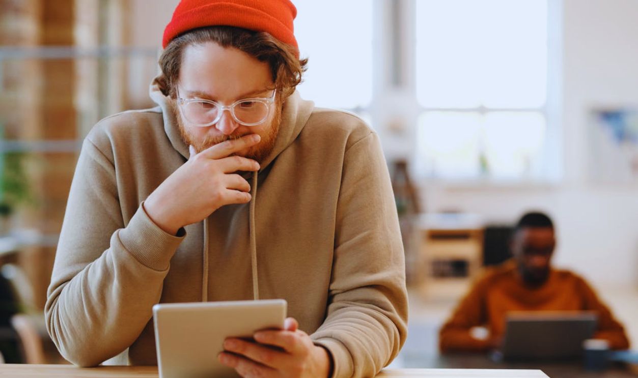 Man in a beanie and glasses using tablet in a bright, modern office.