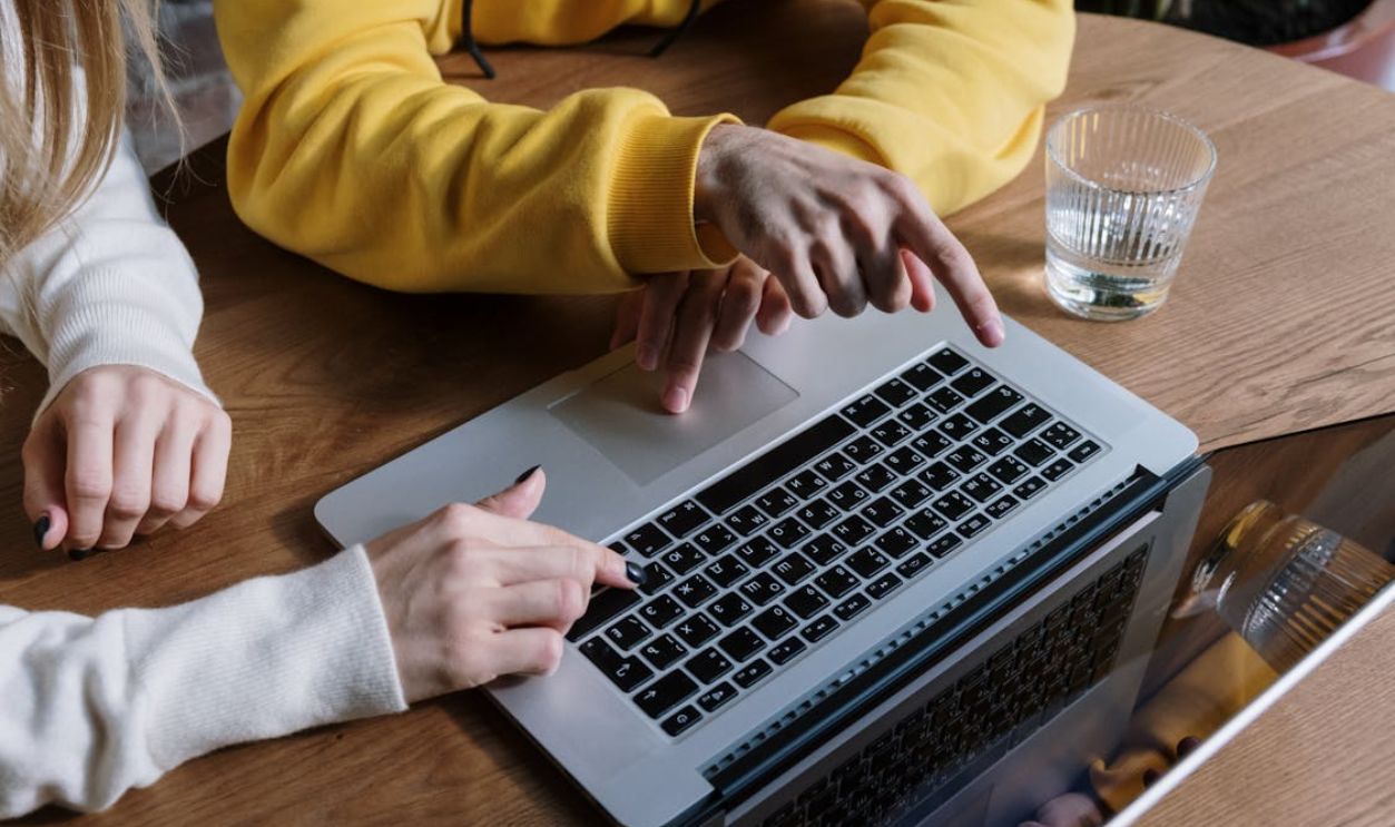 Two people collaborating on a laptop at a wooden table, indicating teamwork and technology use.