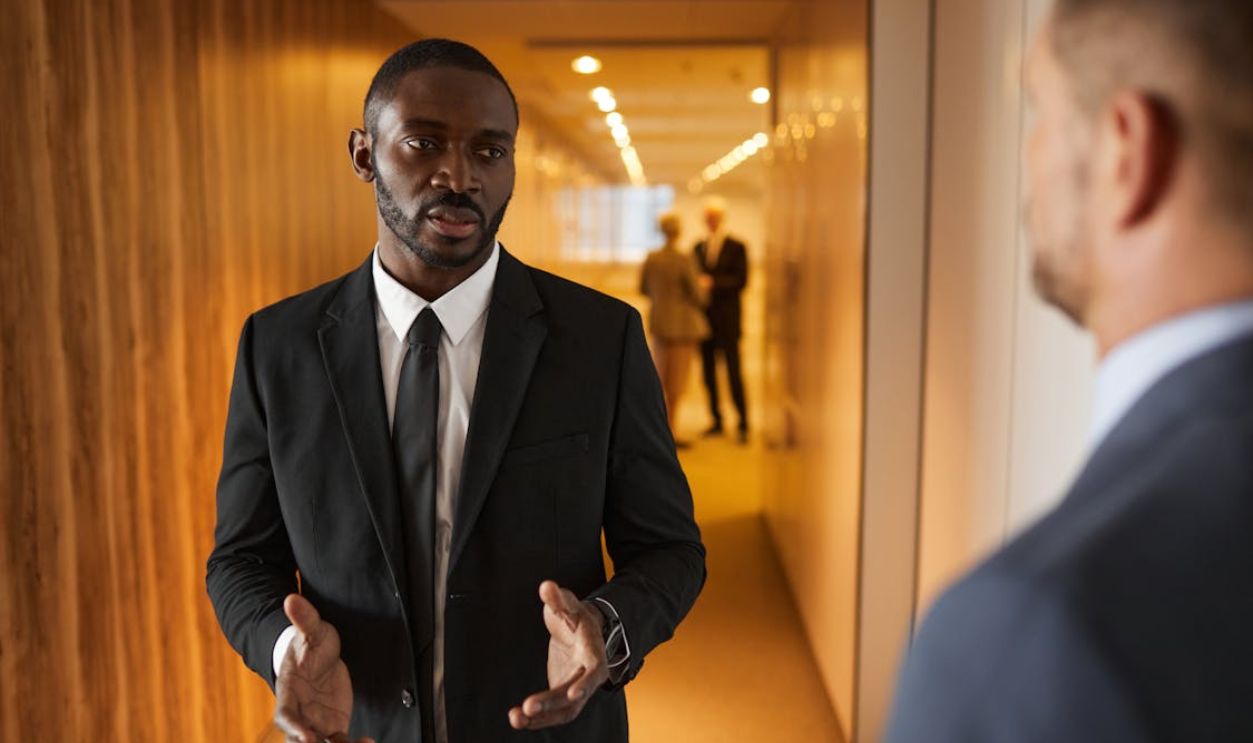 Business professionals in suits having a conversation in a modern office hallway.