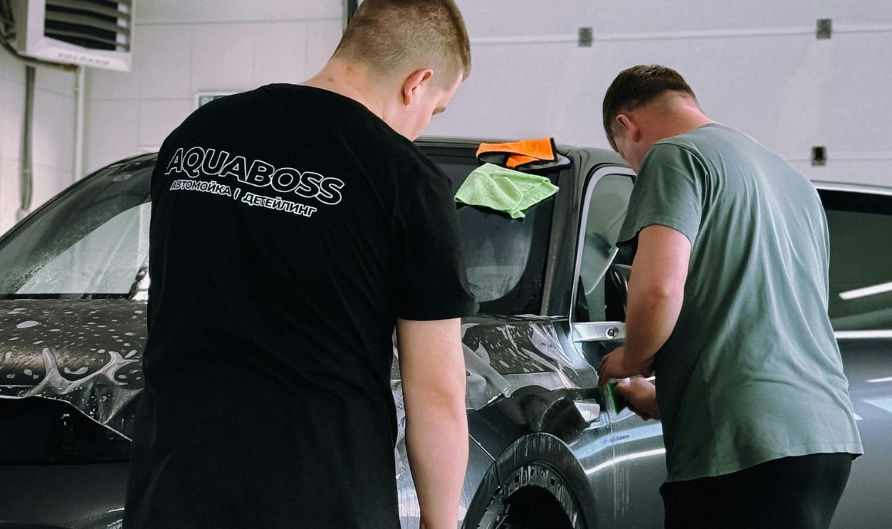 Two men detailing a car in an indoor workshop, focusing on precision and care.