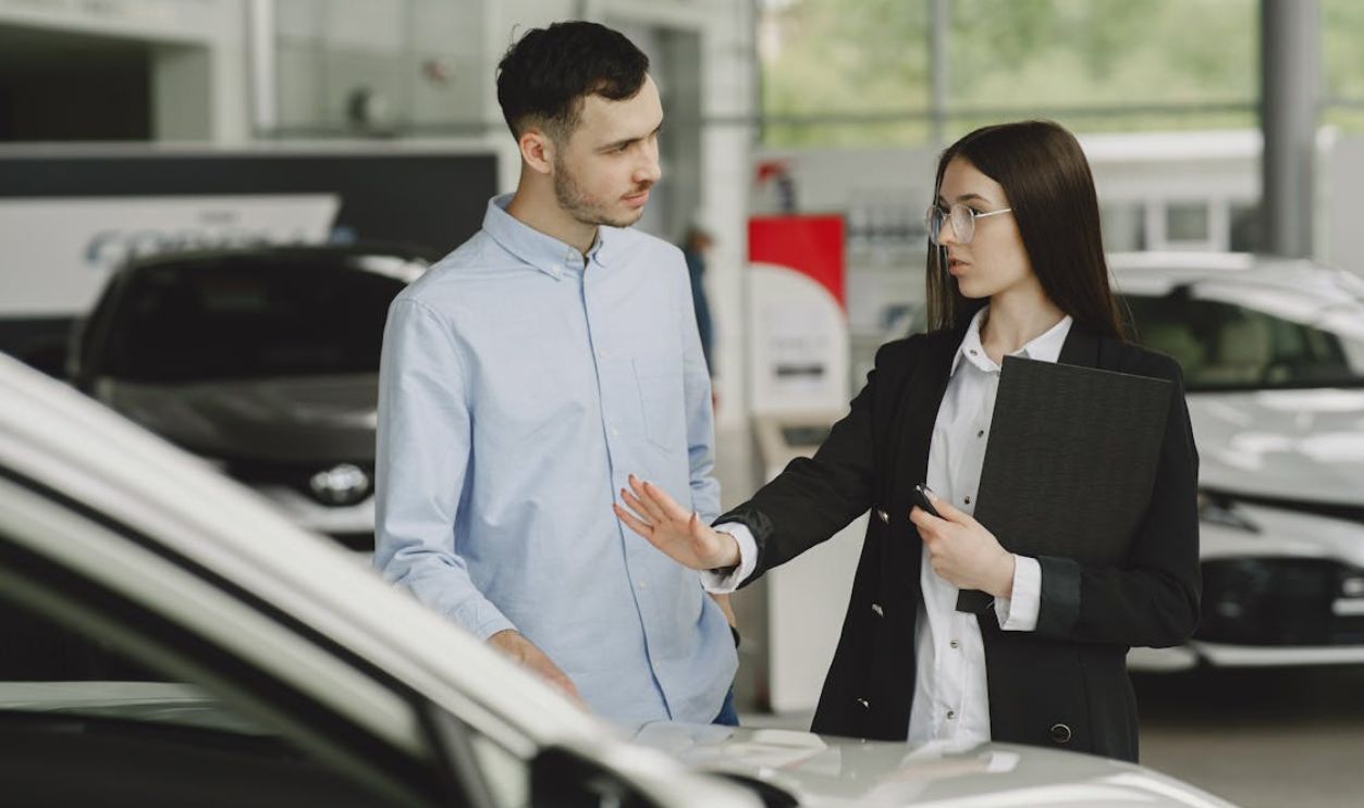 A salesperson and customer discussing car features in a dealership setting.