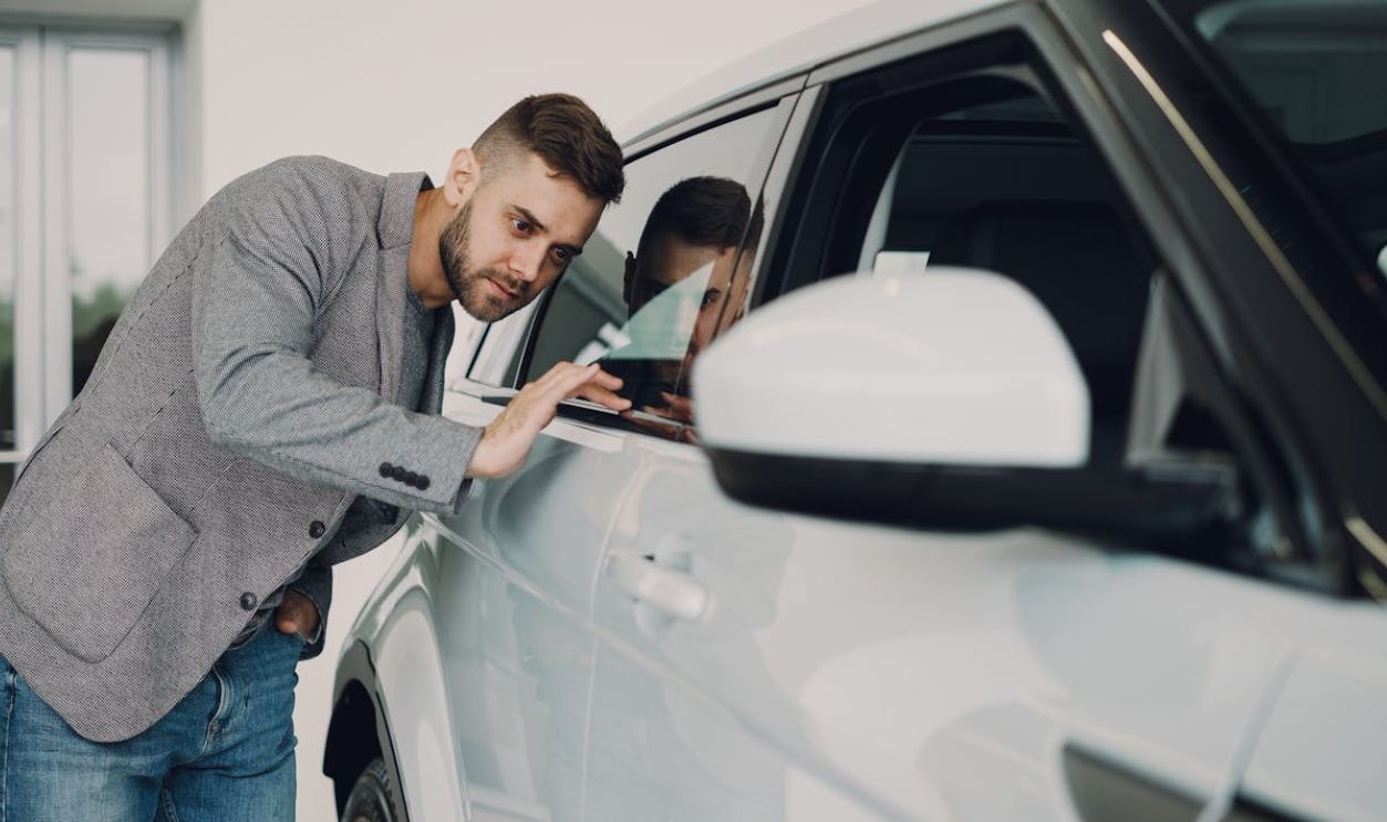 Man carefully examining a modern white car at a dealership showroom.
