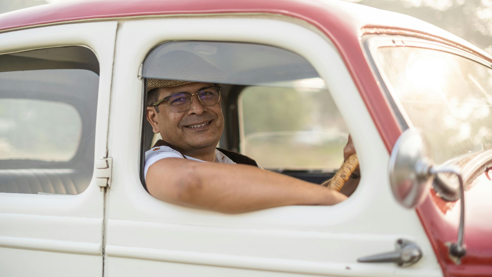 Man in a classic car smiling through the window on a sunny day.