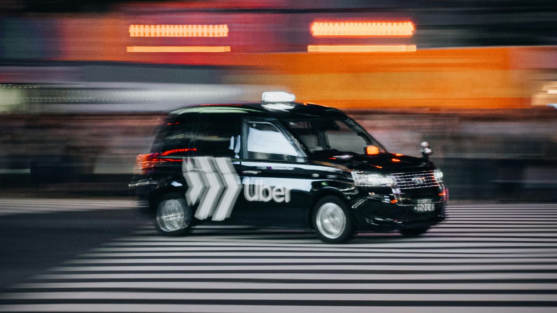Blurred taxi speeds across a city crosswalk, capturing urban motion and nightlife energy.