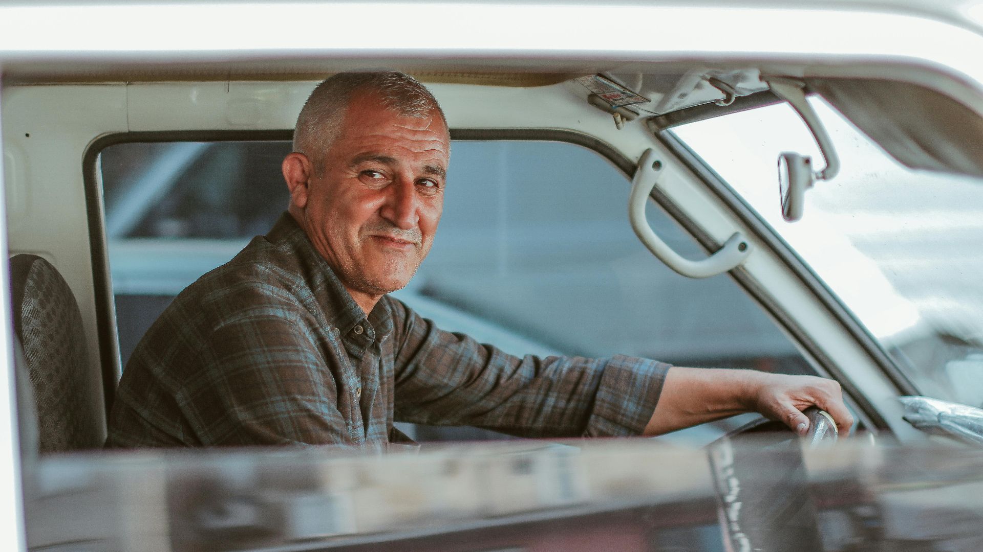 Smiling man driving a vintage vehicle, showcasing a relaxed and confident demeanor.